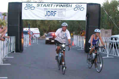Dr. Mandell-Brown crossing the finish line on a bicycle, smiling at the camera