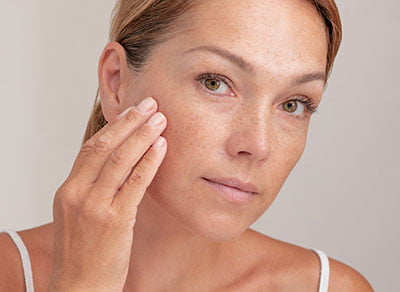 Portrait of cropped caucasian middle aged woman face with freckles touching skin by hand