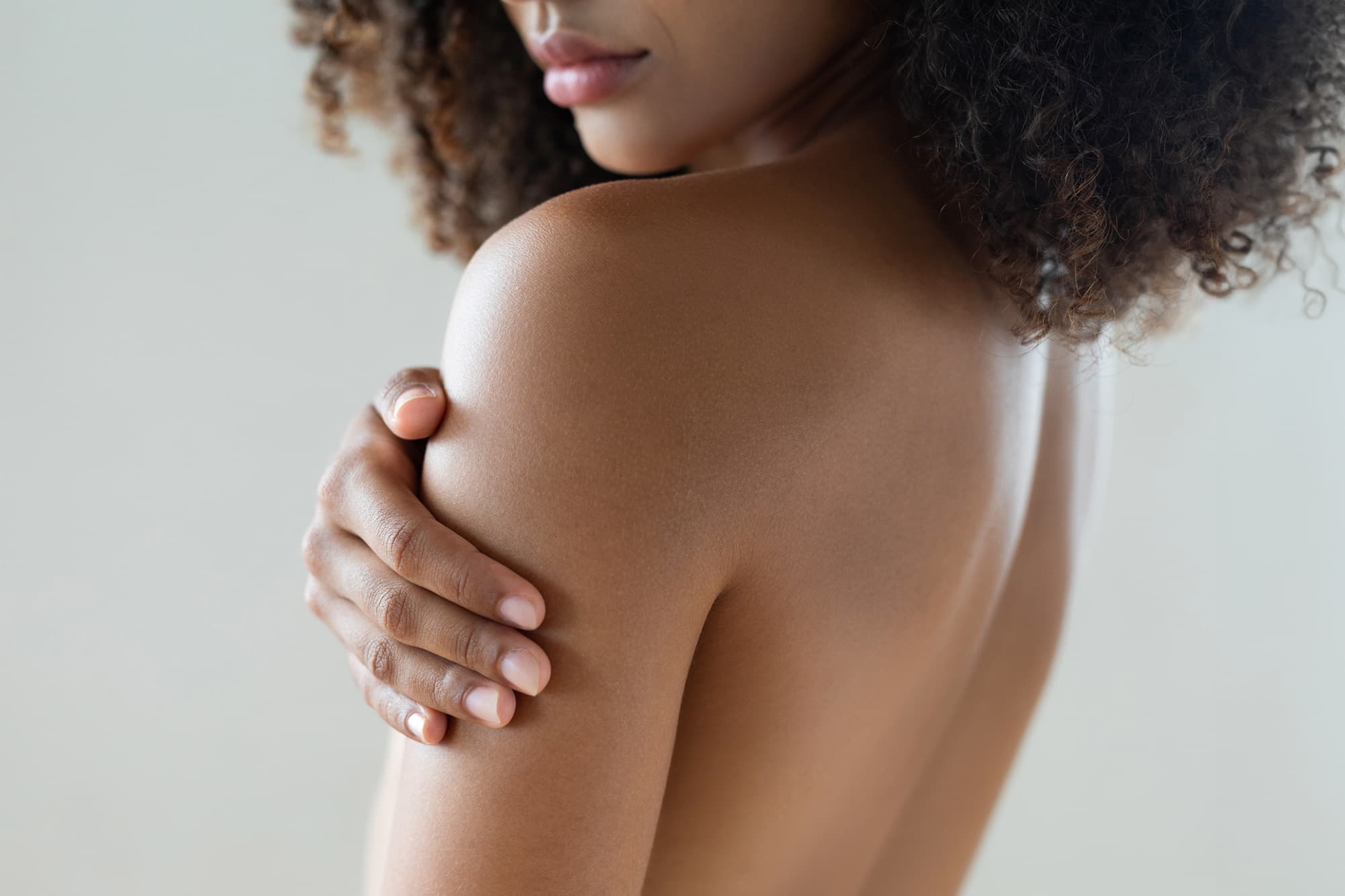 Image of a light skin Black woman look over shoulder, touching her skin