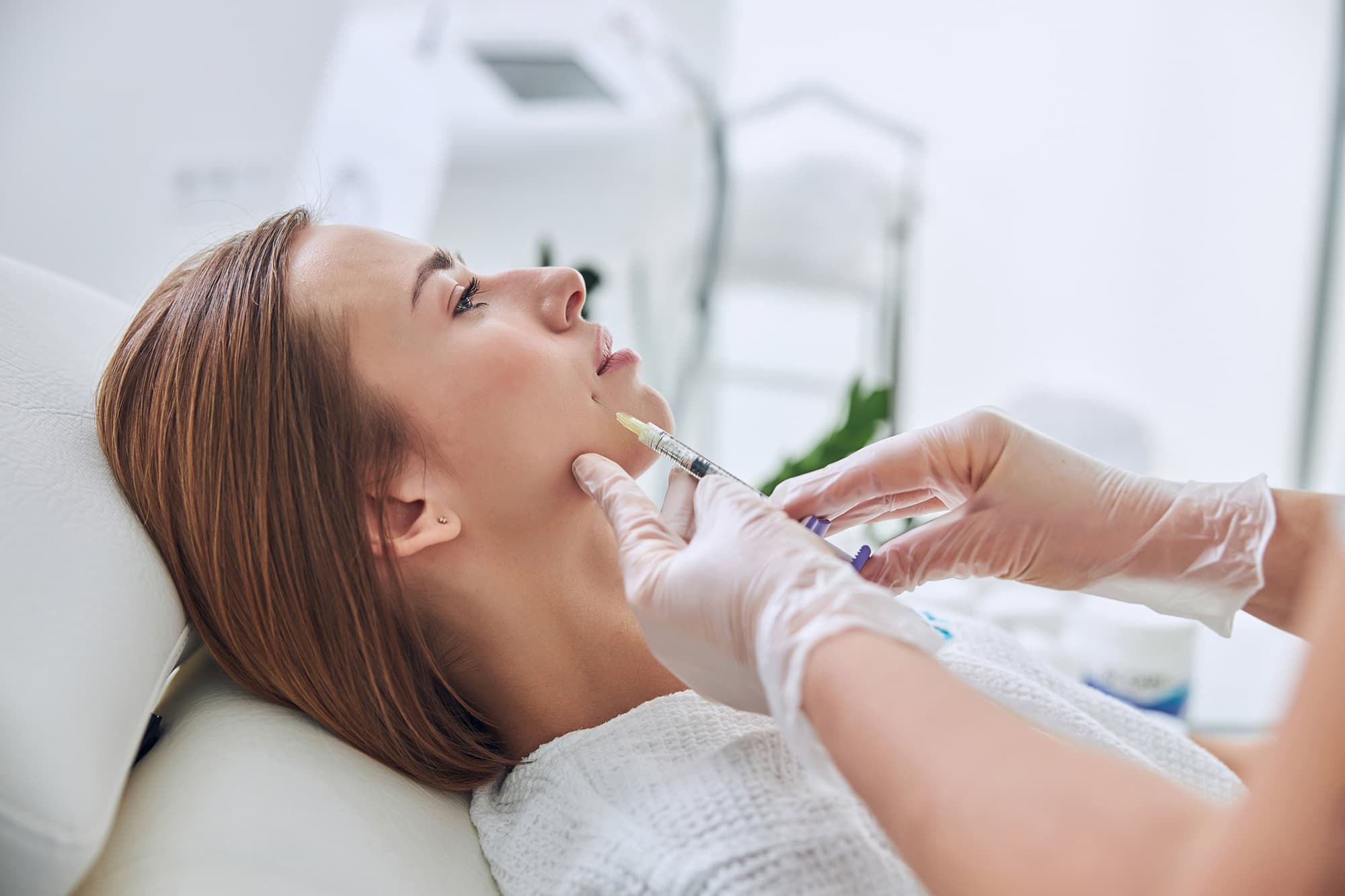 Woman laying in patient chair receiving injectable treatment in lower right cheek