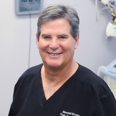 Image of Dr. Mark Mandell-Brown wearing black scrubs and smiling in an operating room