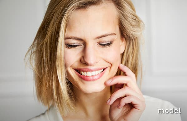 Forehead Lift model of woman looking down smiling with hand in front of left cheek