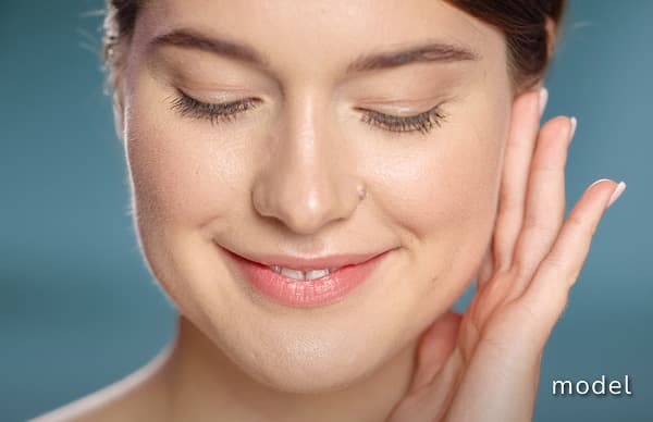 Latisse Eyelash Enhancement model of woman looking down smiling with hand on left cheek