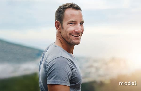 Gynecomastia (Male Breast Reduction) of man outside with head over shoulder smiling at camera