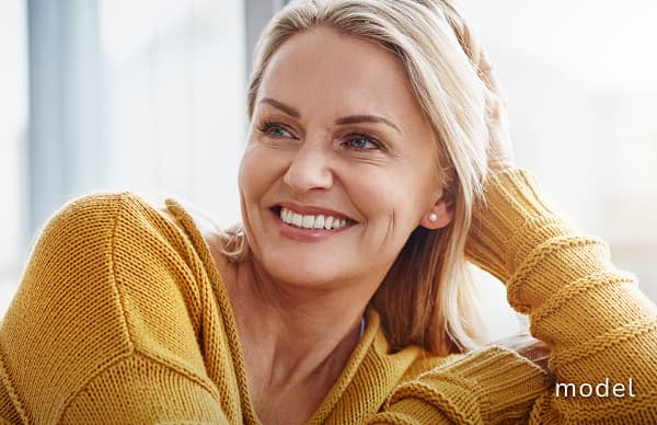 Mid Facelift (Mini Facelift) model of woman sitting wearing yellow sweater smiling away from camera