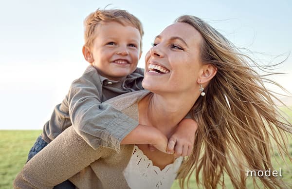 Mommy Makeover model image of woman with child on her back outside in an open field