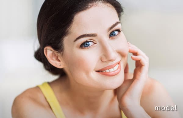 Permanent Makeup model of woman wearing yellow tank top and hand on left cheek