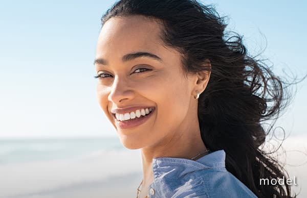 Radiesse® Dermal Filler model image of woman on beach smiling at camera with wind blowing hair