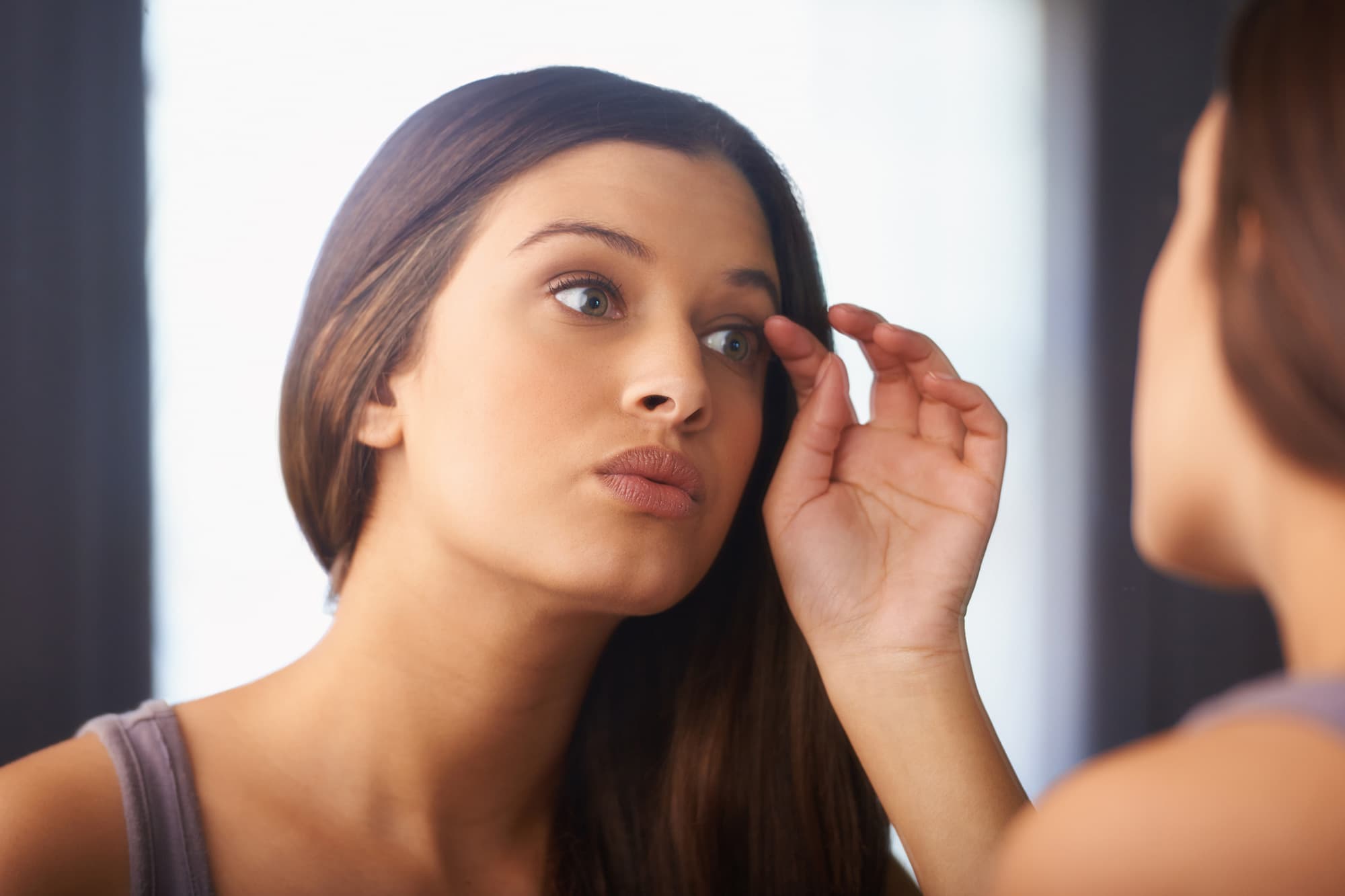Image of a woman looking at her own reflection, touching her eye lashes