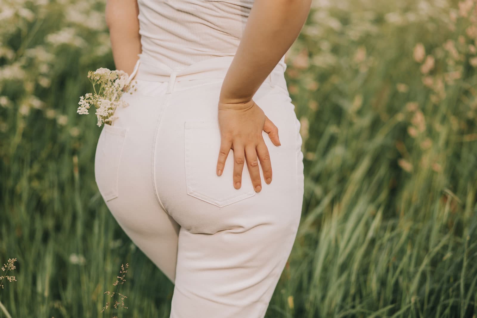 Image of a woman wearing light color denim standing in a field standing away from the camera. The image is cropped to focus on the woman's buttocks.