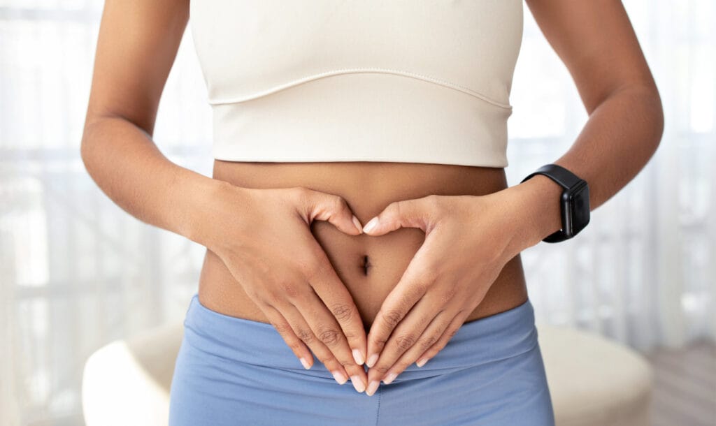 Faceless woman in sportswear doing heart sign with hands on stomach